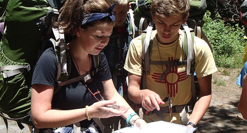 Two people wearing backpacks examine a map.